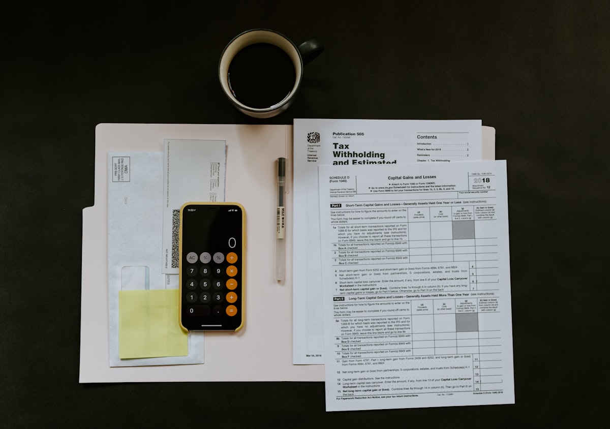 Bank statements and tax forms on a desk beside a calculator and a cup of coffee